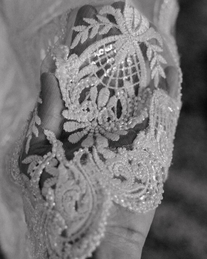 Close-up detail of delicate white lace embroidery pattern on fabric in black and white.