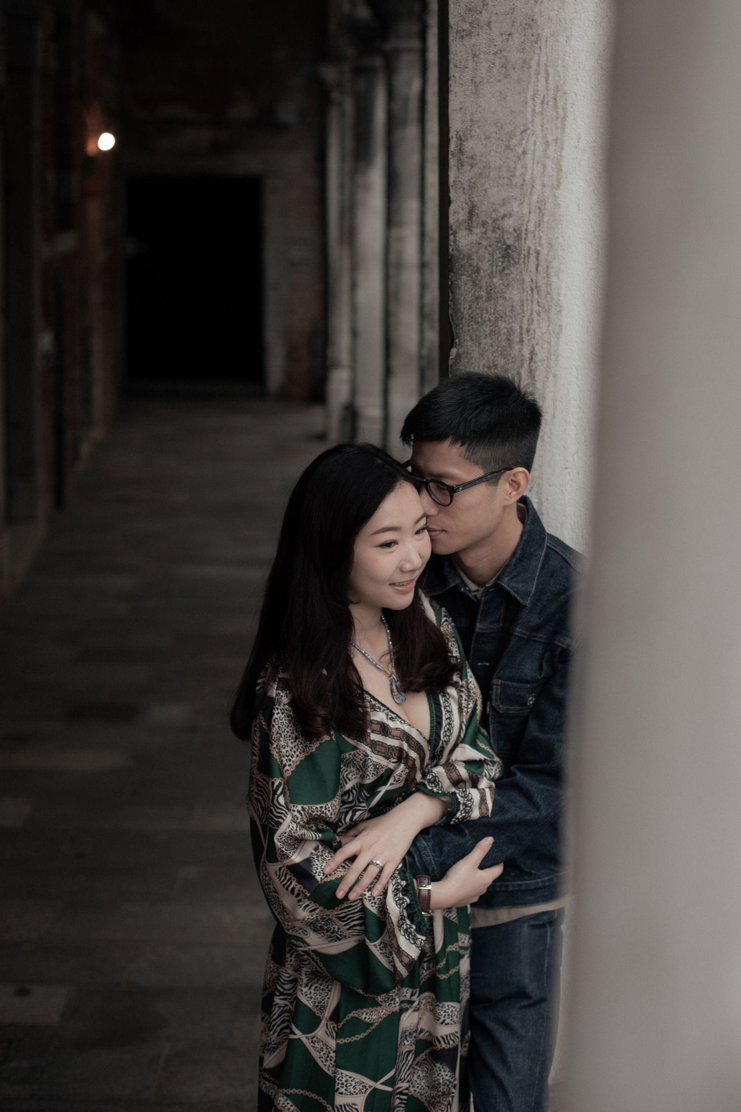 Romantic portrait of a couple holding each other in a softly lit Venetian corridor.