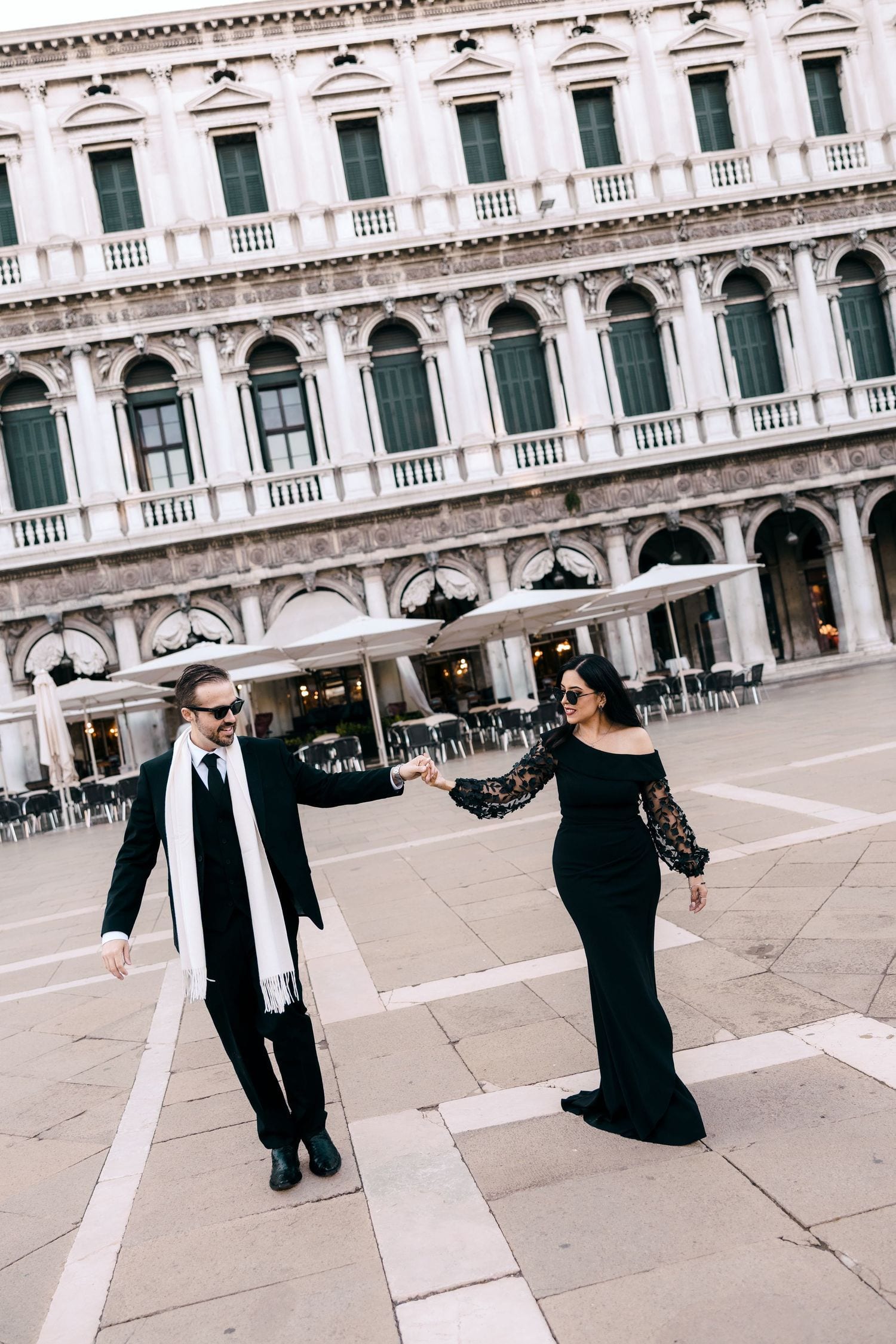 Elegant couple in black walking hand in hand across Piazza San Marco