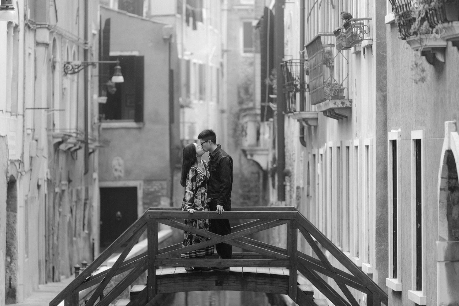 Black and white couple portrait on a wooden bridge over a narrow Venetian canal.
