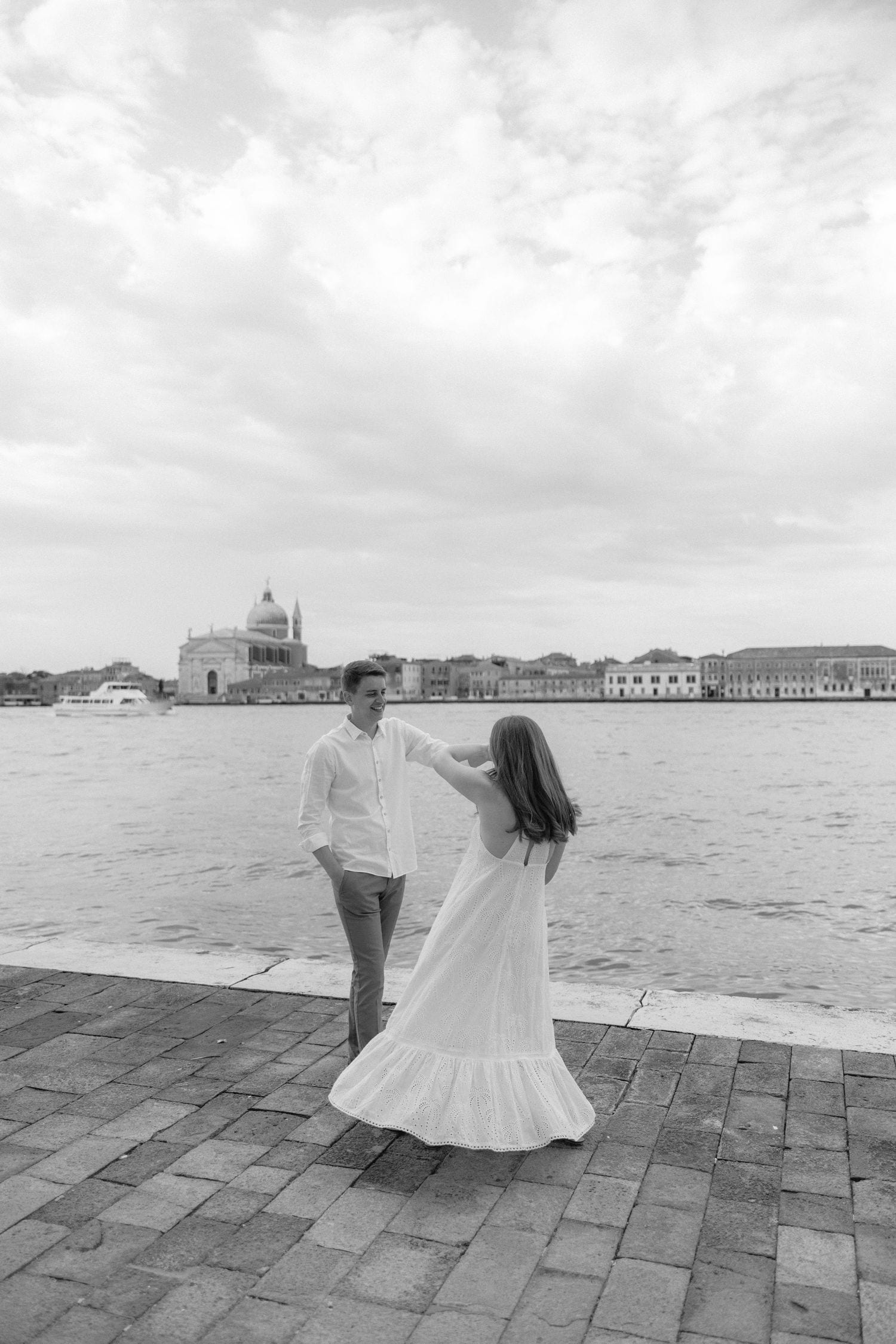 A dreamy black and white scene with flowing white dress on cobblestone by Venice canal and architecture in background.