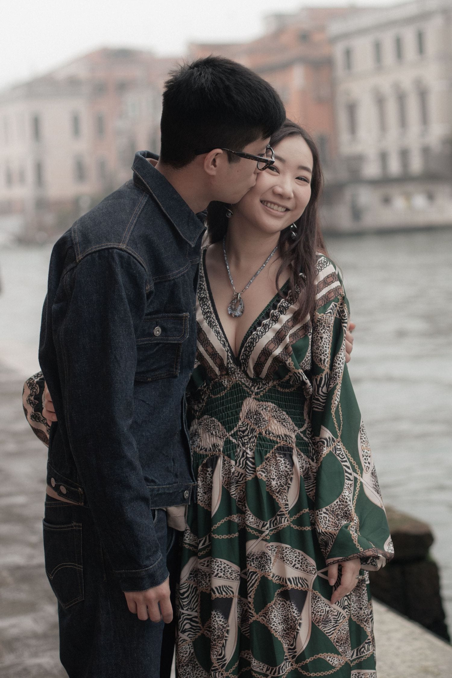 Man kissing his partner on the cheek during a romantic couple photoshoot by the Grand Canal.