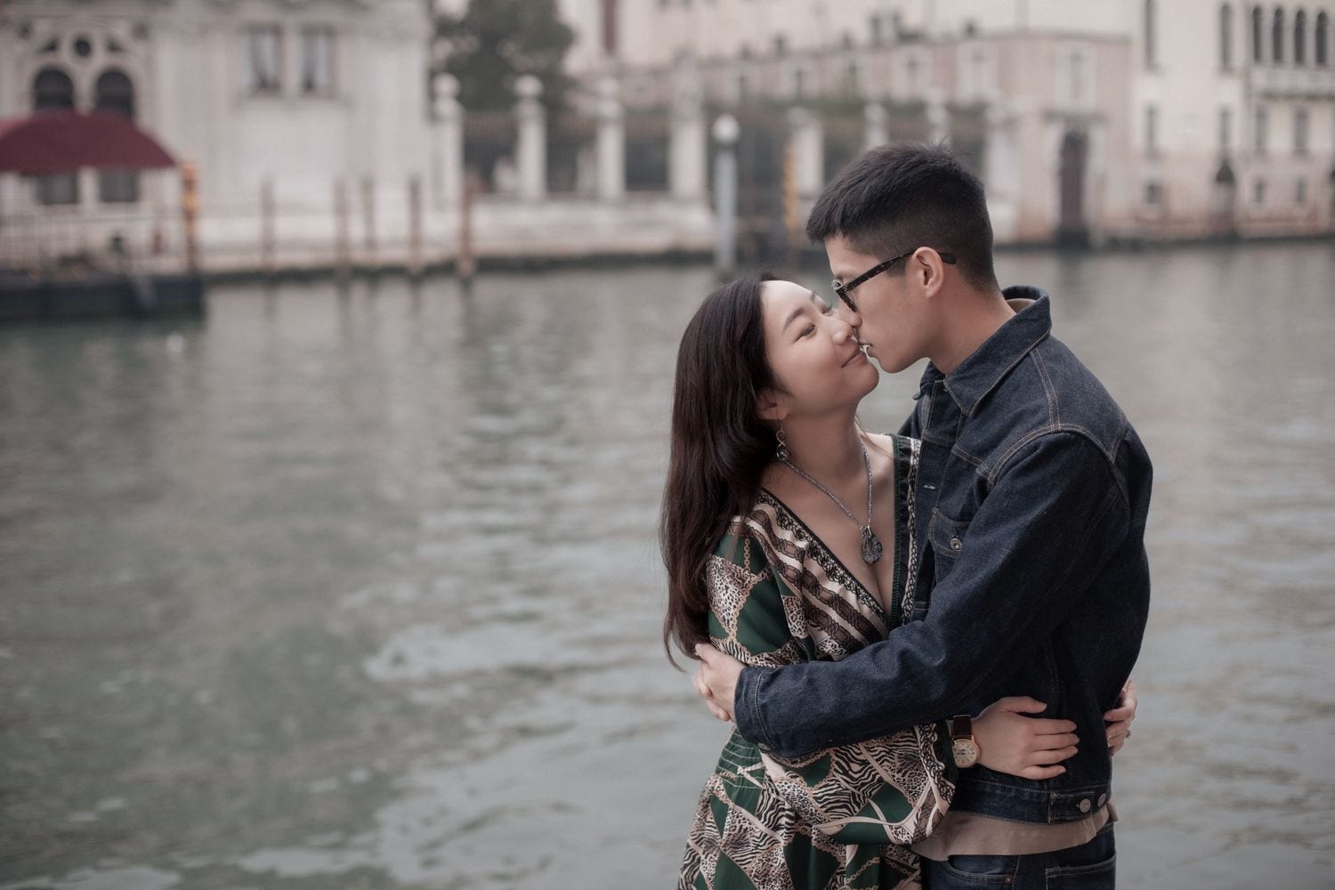 Couple sharing a gentle kiss by the water during a romantic photoshoot in Venice.