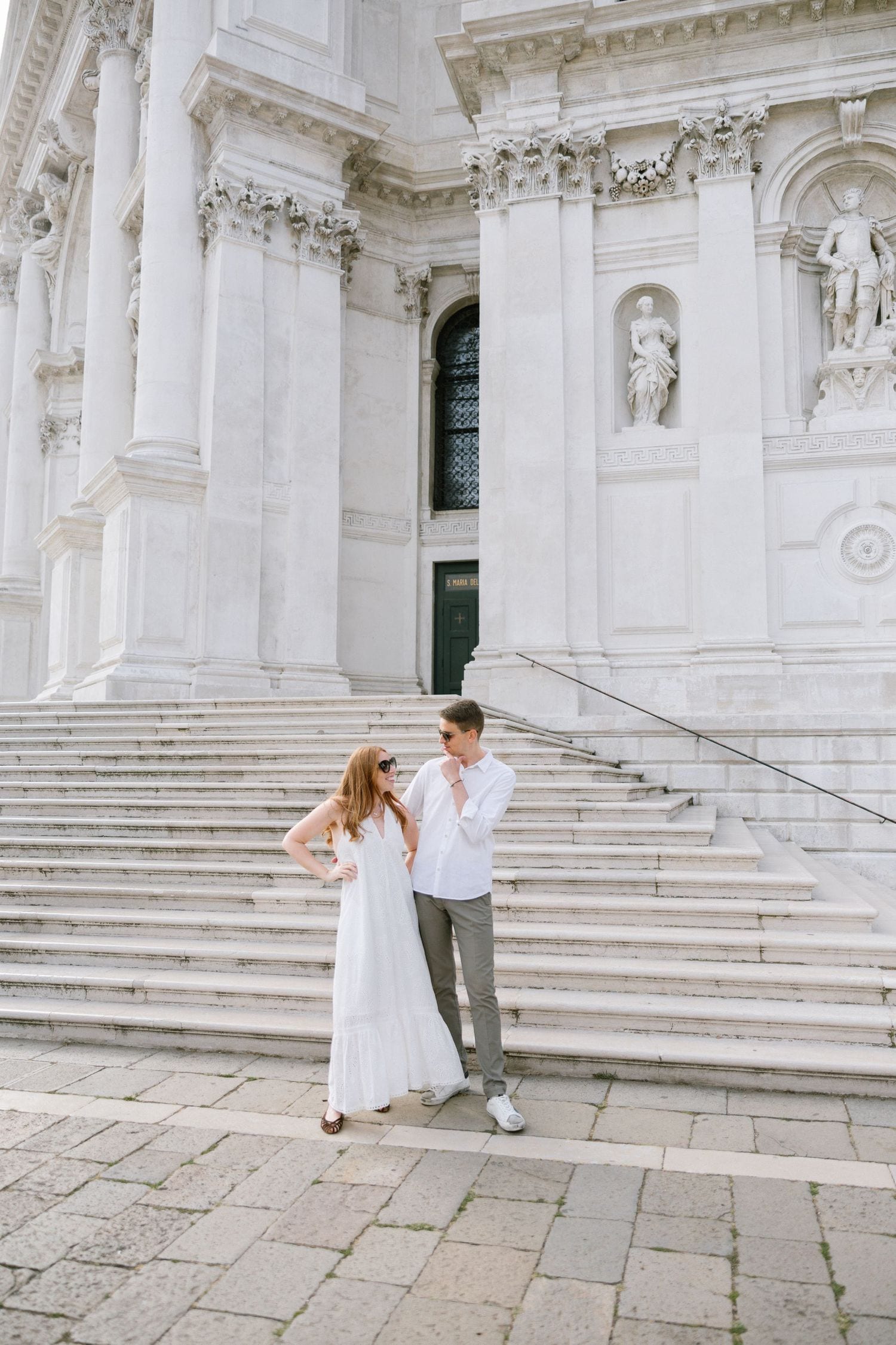 A couple poses on the grand white marble steps of a historic Venetian building.