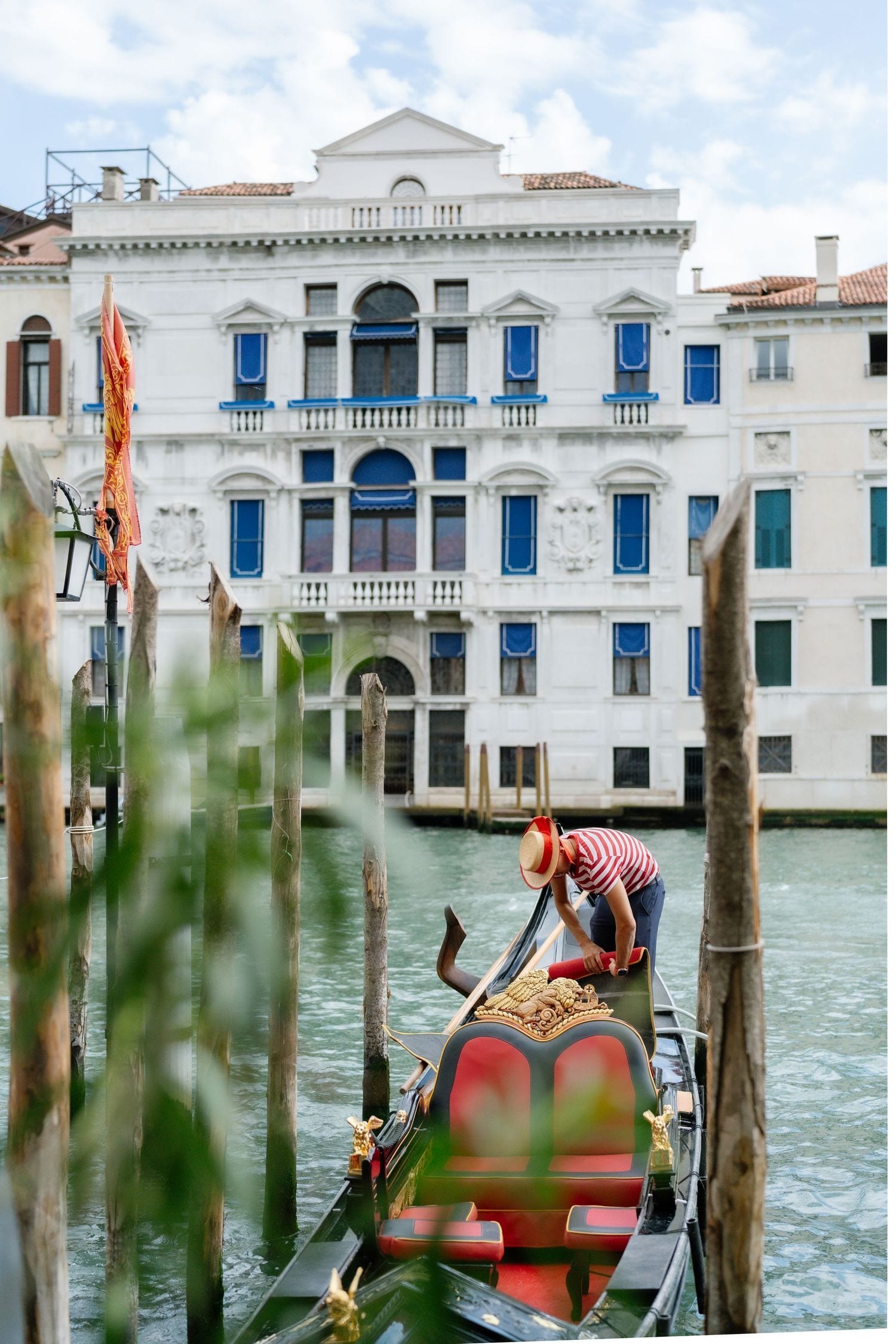 Traditional gondola being prepared on Venice's Grand Canal with historic white palazzo building featuring blue shutters in background.