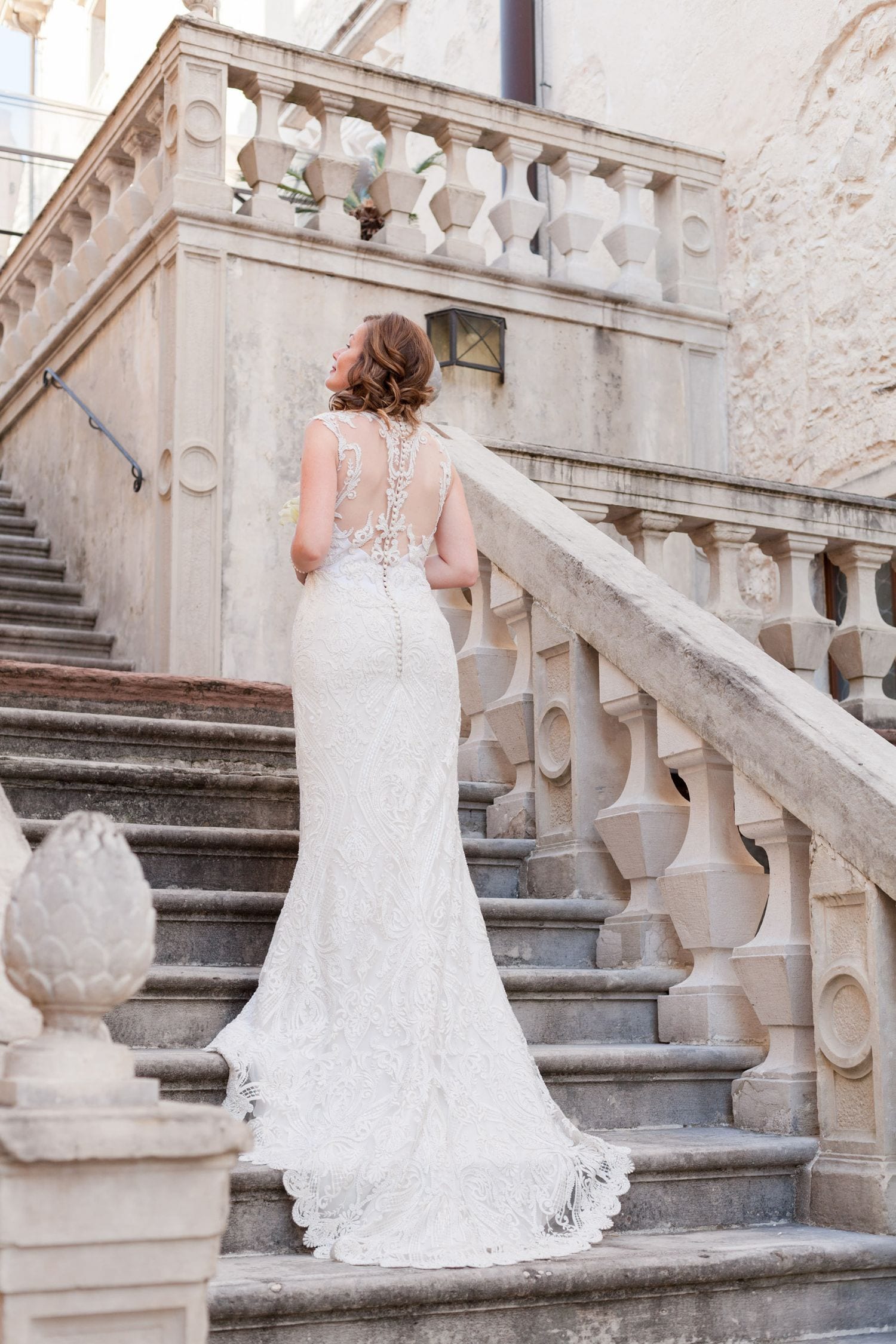 An elegant lace wedding dress with illusion back details photographed from behind on grand stone stairs.
