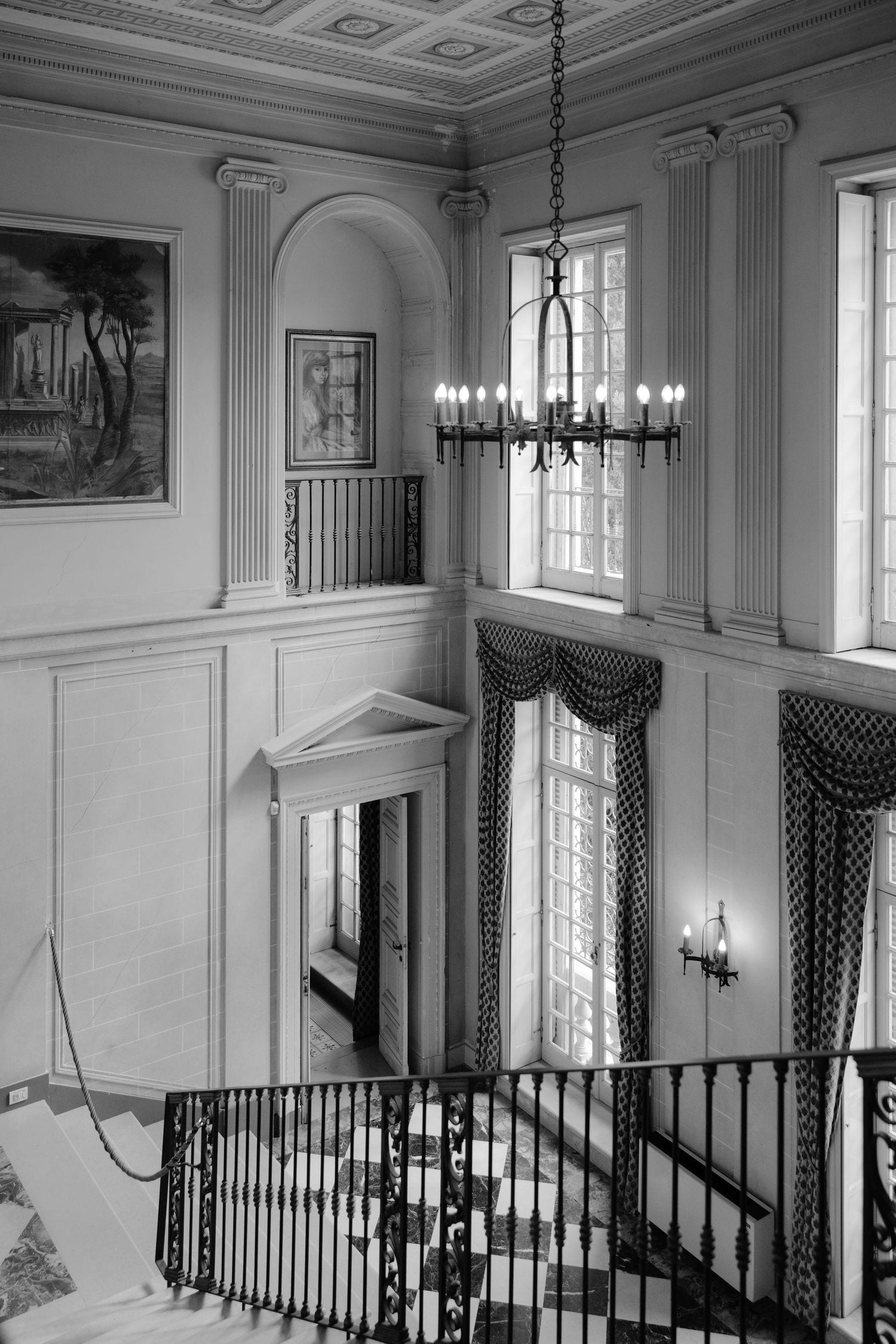 Scala elegante con lampadario e finestre drappeggiate in una dimora storica.