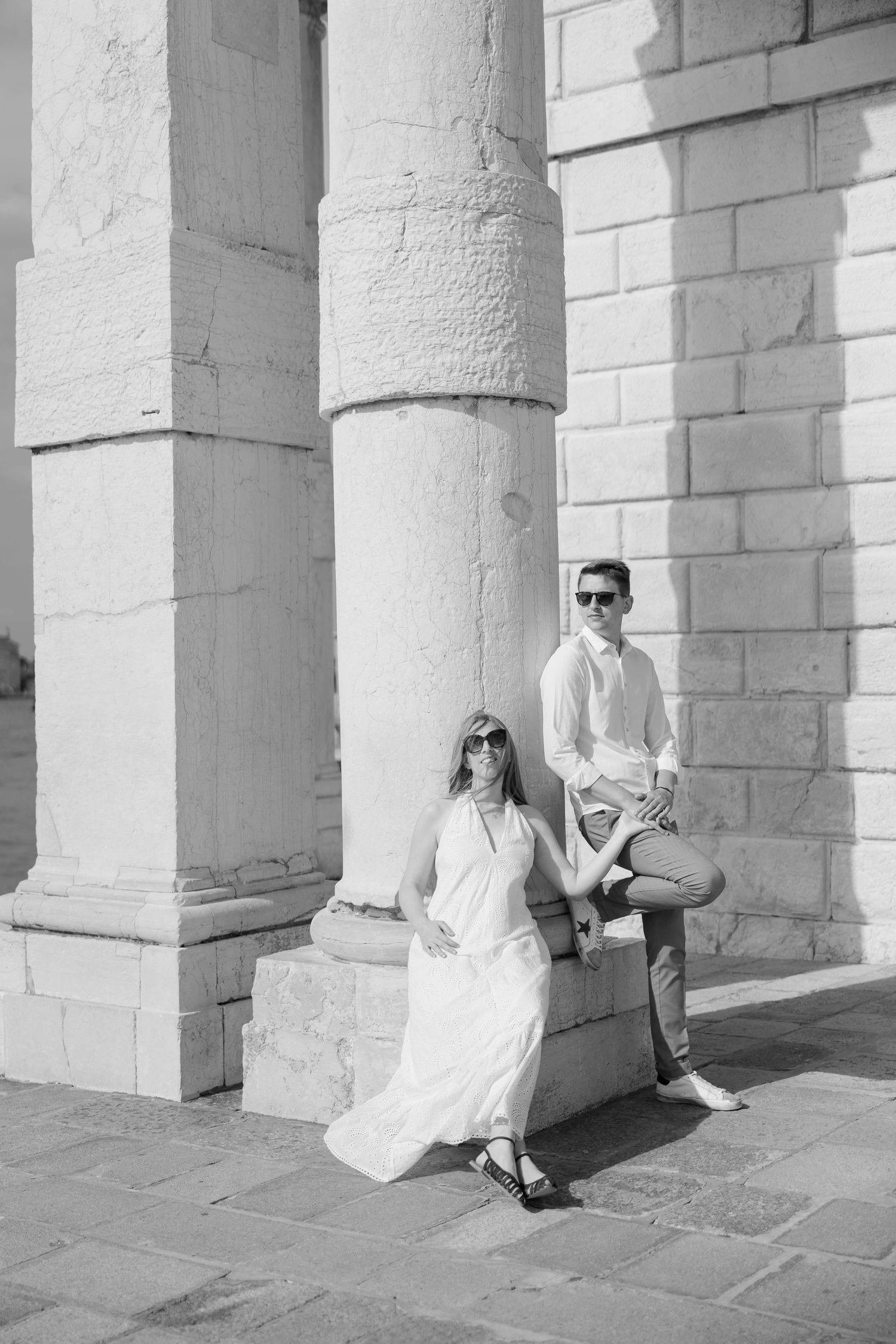 A couple poses between white stone columns of a historic Venetian building.