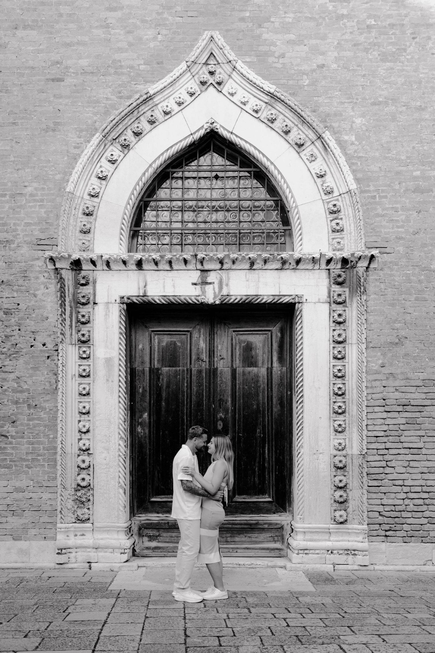 Black and white portrait of a couple embracing before an ornate Gothic doorway in Venice