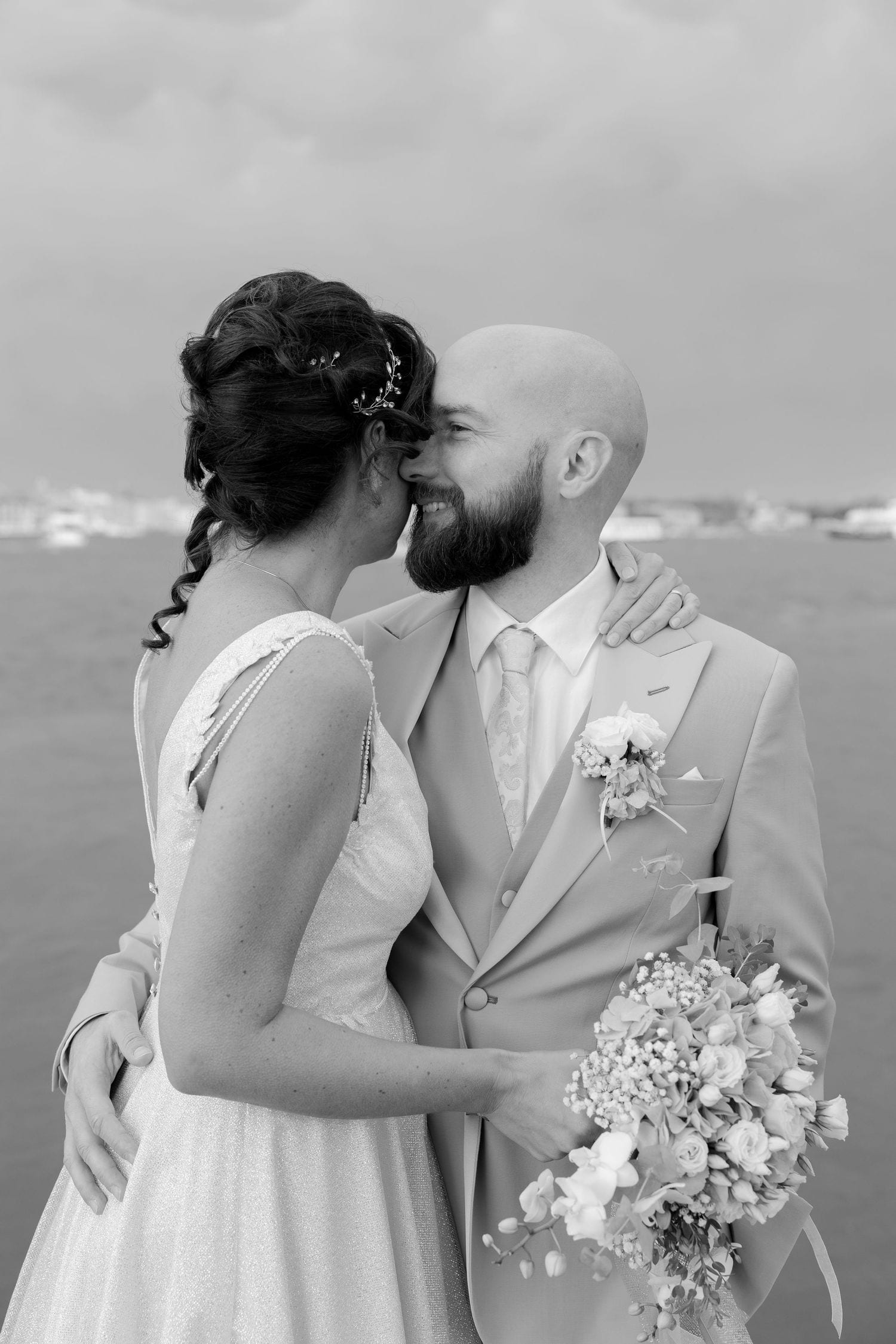 A romantic black and white wedding portrait featuring a couple sharing an intimate moment with a bridal bouquet.