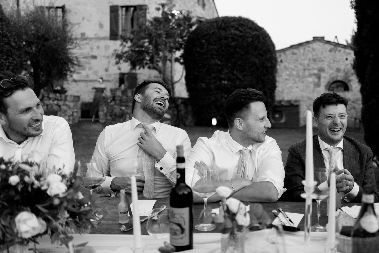 Amici e famiglia che ridono durante il ricevimento all’aperto.