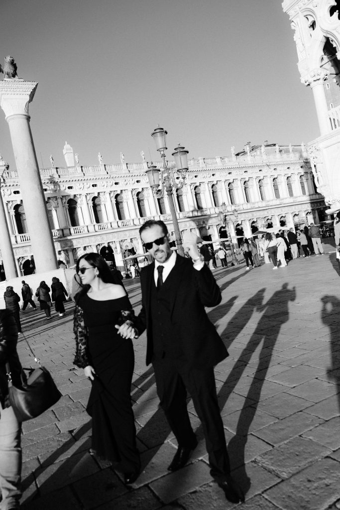 Black and white portrait of a couple walking through Piazza San Marco with long morning shadows