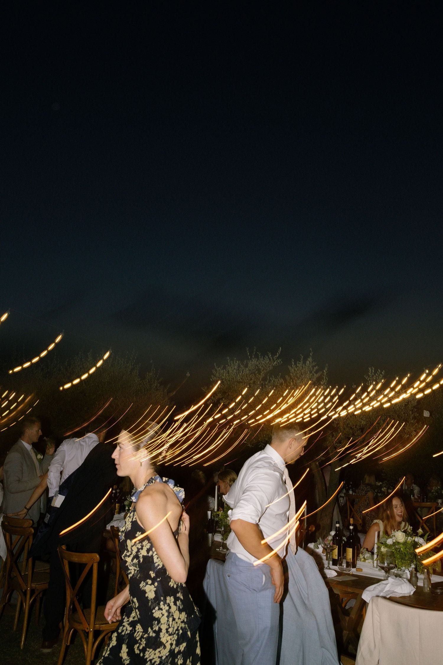 Luci sospese che creano atmosfera durante una cena di matrimonio all’aperto in Toscana.