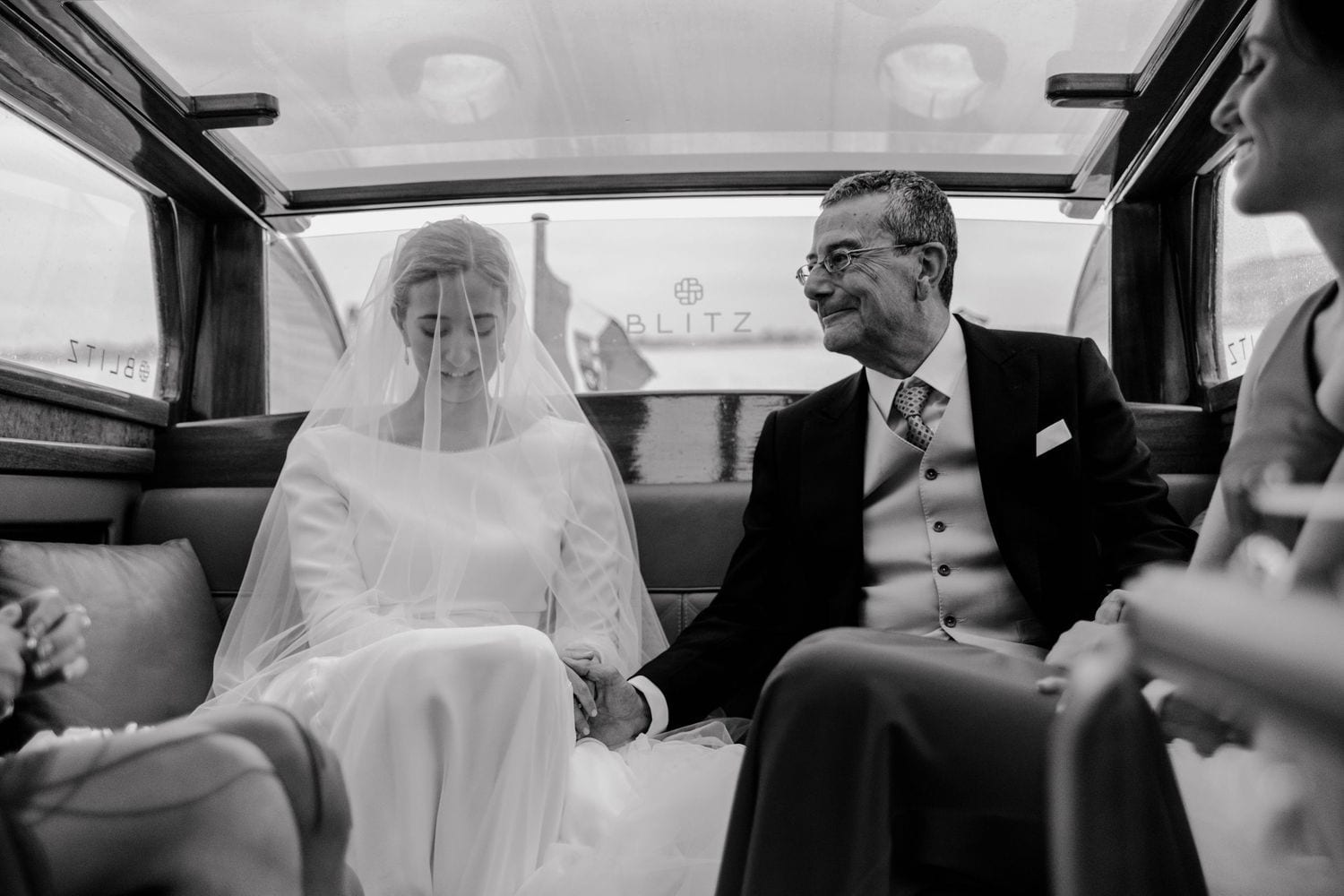 Black and white photo of bride and groom holding hands and smiling at each other while seated in a Blitz taxi
