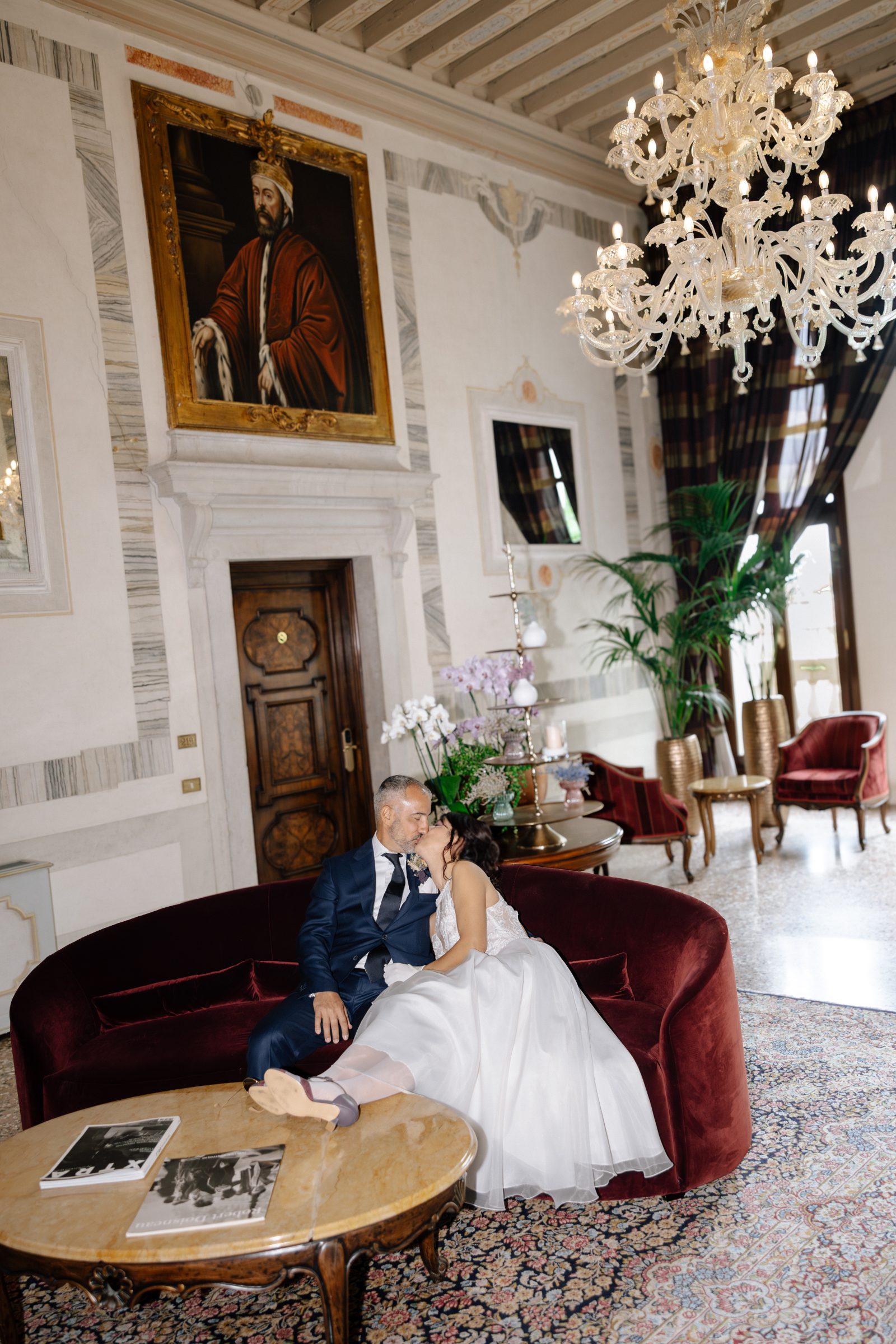 Newlyweds in a Venetian room with a red sofa during their small wedding reception