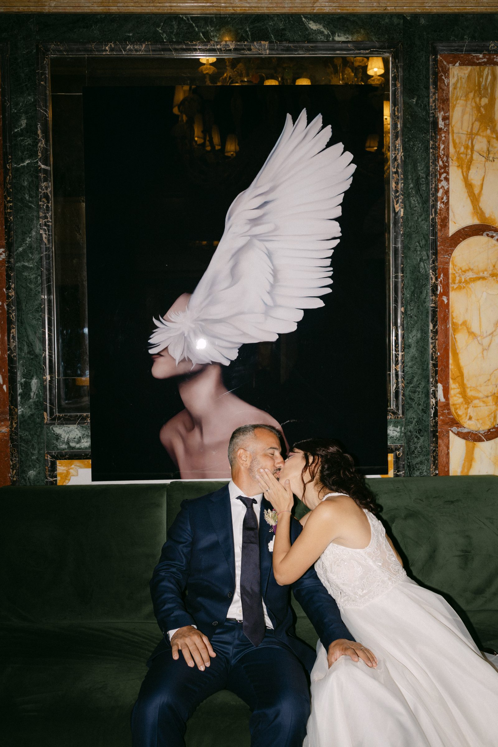 Newlyweds kissing beneath a feathered artwork during their intimate Venice reception