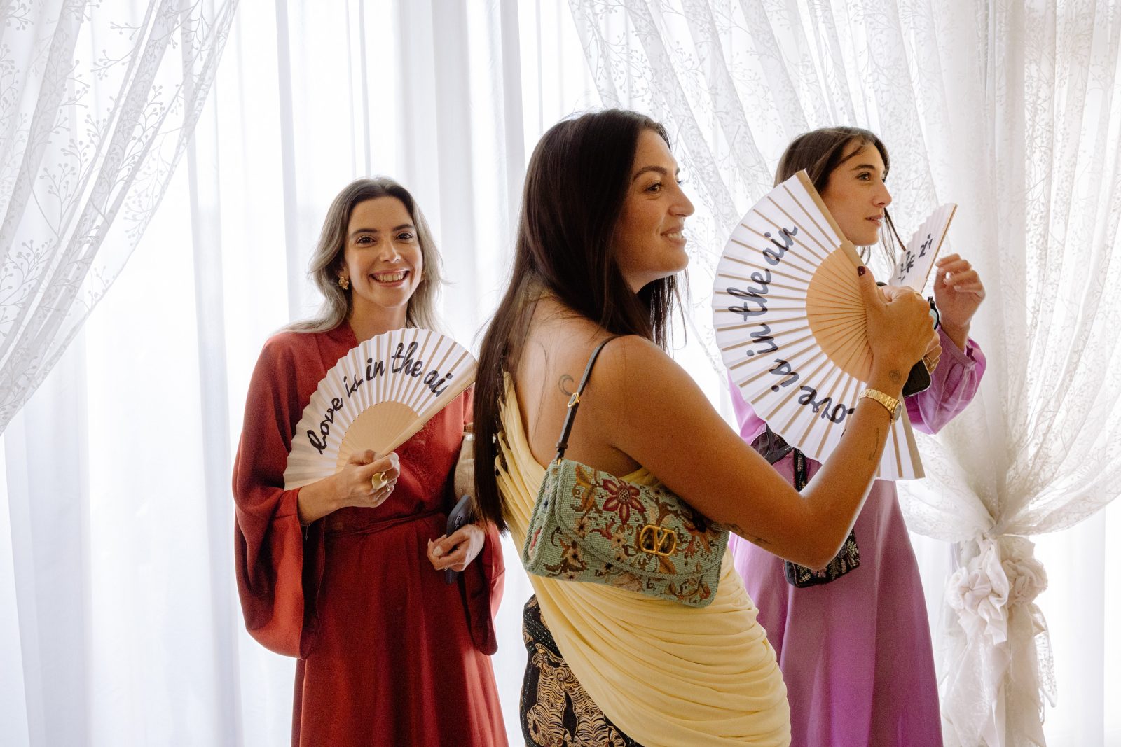 Invitate con ventagli accanto a una tenda chiara