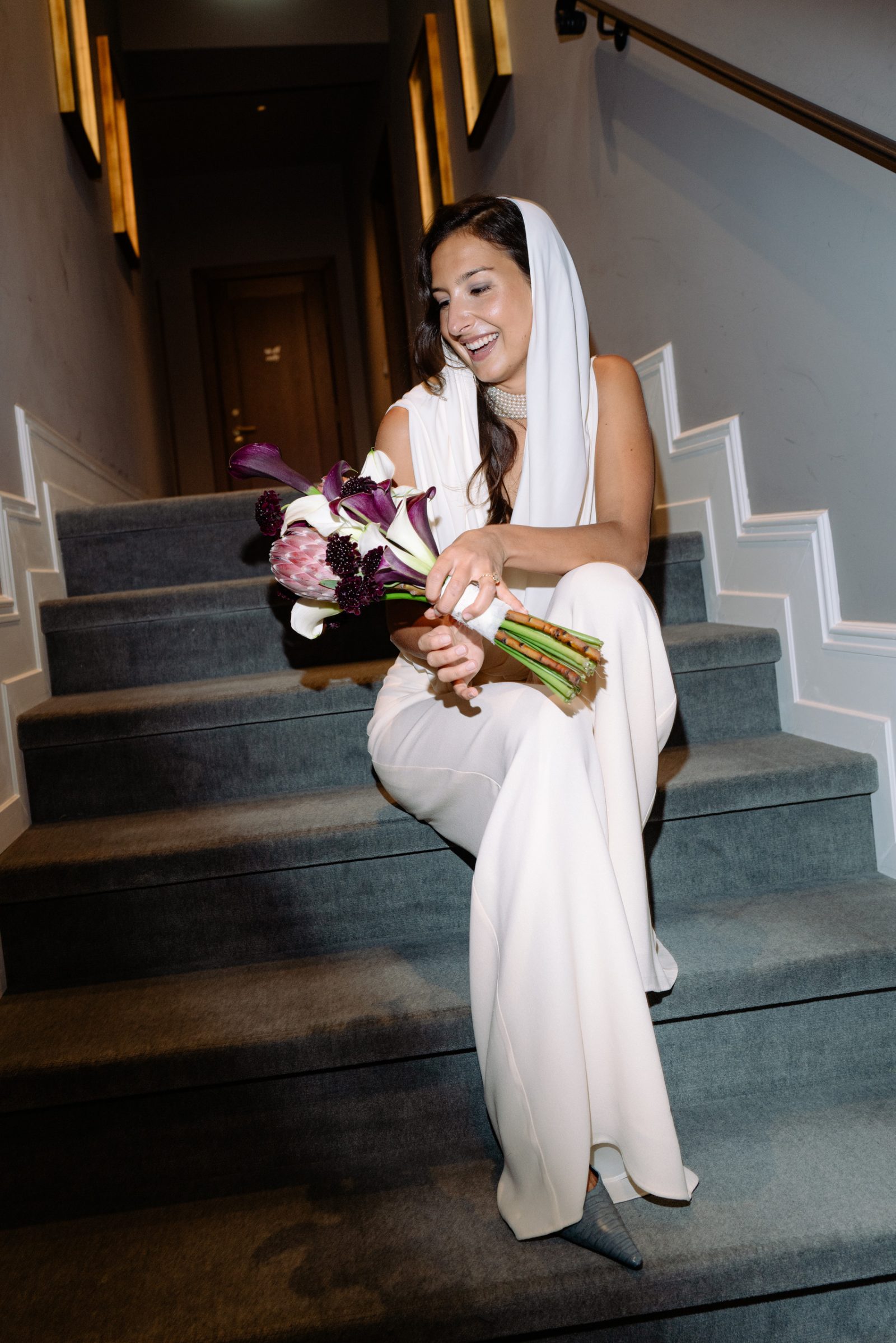 Allegra sorride seduta su una scala con il bouquet